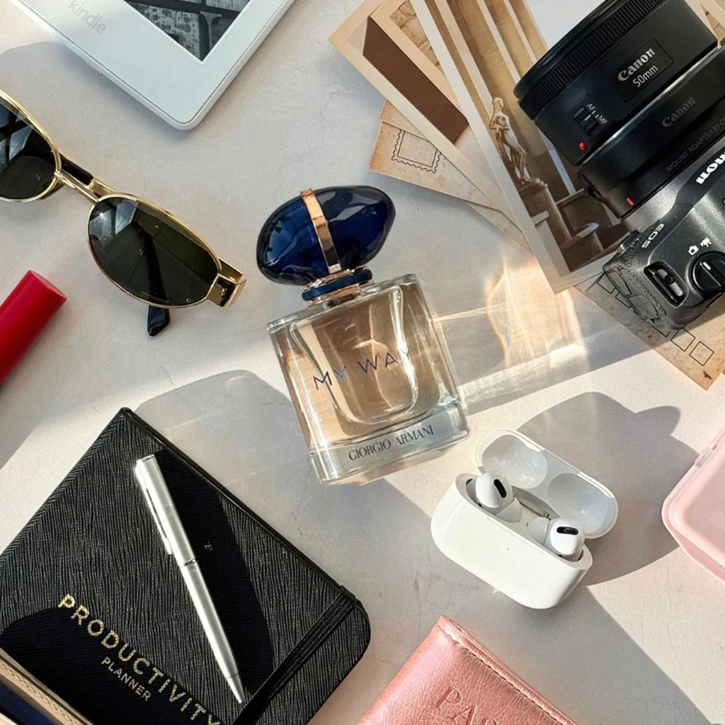 Perfume bottle, sunglasses, camera, and other items on a light surface